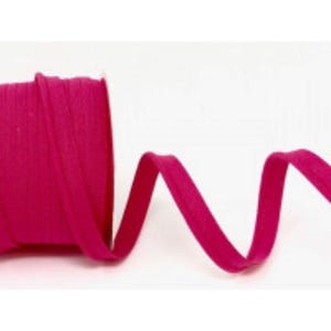 May include: A roll of bright magenta bias tape, partially unrolled, against a white background. The tape is folded over, creating a clean edge. The tape is likely used for sewing and crafting projects.