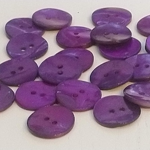 Könnte beinhalten: Eine Sammlung von violetten Muschelknöpfen mit jeweils zwei Löchern. Die Knöpfe haben ein marmoriertes Muster und eine glatte Oberfläche.