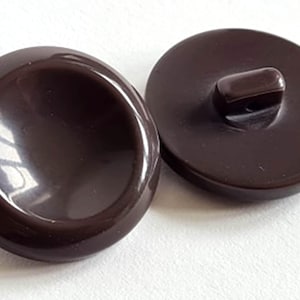 May include: Two brown plastic buttons with a raised centre. One button has a shank on the back.