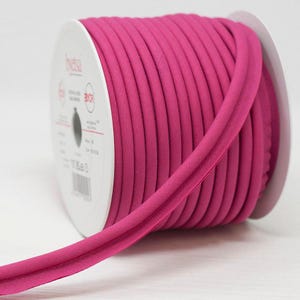 May include: A roll of bright pink bias binding, ideal for sewing and craft projects. The binding is tightly wound on a white cardboard reel, with a section unwound and visible. The binding is a vibrant fuchsia colour.
