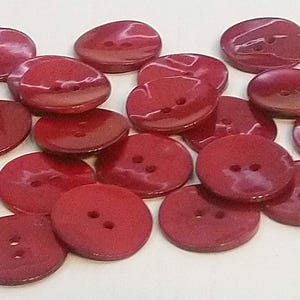 May include: A collection of red, round buttons with two holes each. The buttons are made of a shiny, smooth material.