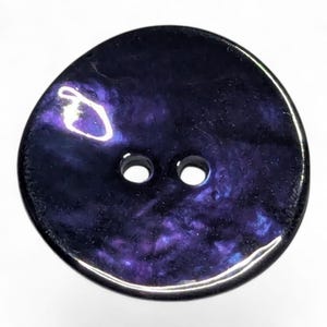 May include: A circular button in dark purple, featuring two holes. The button has a glossy surface with swirling patterns of lighter purple and blue. The button's shape is slightly irregular.