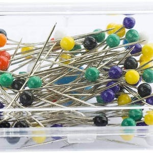 May include: A clear plastic container filled with colorful sewing pins. The pins have round heads in various colors, including red, yellow, green, blue, and black.