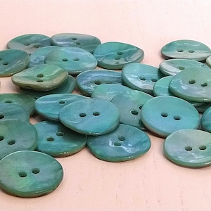 May include: A pile of teal and green iridescent buttons. The buttons are oval shaped and have two holes.