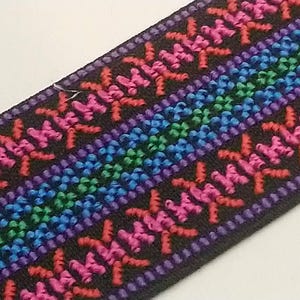 May include: Black elastic trim with a colourful geometric pattern. The pattern features pink, red, blue, green, and purple thread.