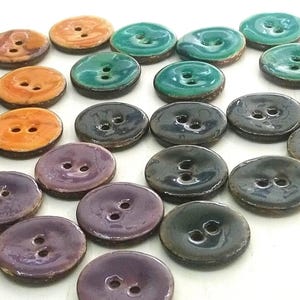May include: Assortment of ceramic buttons in various colours, including teal, green, purple, and orange. The buttons are oval-shaped and have two holes.