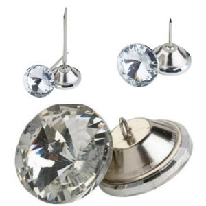 Op de afbeelding: Close-up van transparante kristallen stofferingsspelden met zilveren metalen bases en een pin om aan stof te bevestigen. De spelden hebben een facetgeslepen ontwerp.