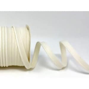 May include: A roll of white cotton bias binding, a type of fabric trim, is shown on a white surface. The binding is folded in half and is approximately 2.5 cm wide.