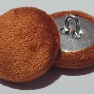 Könnte beinhalten: Zwei braune Samtknöpfe mit einem Metallstiel. Die Knöpfe sind rund und haben eine weiche, flauschige Textur.
