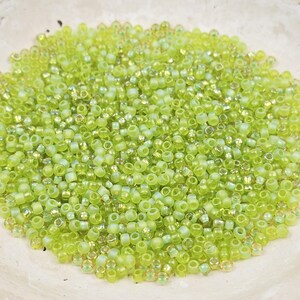 May include: A collection of small, round, translucent lime green glass seed beads. Each bead features a smooth, polished surface with a consistent circular shape and a central hole, creating a vibrant, uniform pile of bright green crafting components.