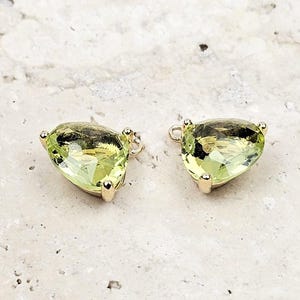 May include: Two pear-shaped, light green faceted gemstones set in gold metal frames. Each gemstone features a small gold jump ring attached to the top, designed for use as a jewelry charm or pendant component for necklaces or earrings.