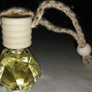 May include: A clear glass bottle with a diamond-shaped design, filled with a light yellow liquid. The bottle has a wooden cap with a string attached for hanging.