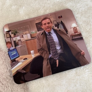 Può includere: Un tappetino per mouse rettangolare con una scena di The Office. Un uomo con un trench beige e una cravatta a motivi geometrici tira fuori la lingua aprendo il cappotto. Sullo sfondo, un ufficio con scrivania, monitor e un collega.
