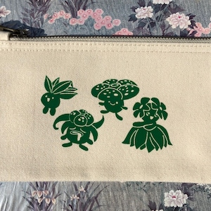 Peut inclure: Une pochette zippée en toile blanche avec un imprimé vert de quatre personnages de dessin animé. Les personnages sont un champignon, une fleur et deux autres créatures.