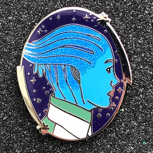 May include: A blue and green enamel pin featuring a profile of a person with blue hair and a starry night background.