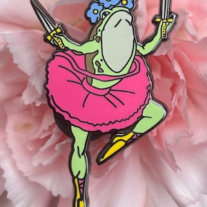 May include: A green frog wearing a pink tutu and a crown of blue flowers, holding two silver swords, with yellow shoes.