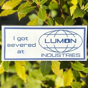 May include: A white sticker with blue text and a blue logo. The text reads "I got severed at LUMON INDUSTRIES". The logo is a blue globe with the word "LUMON" inside.