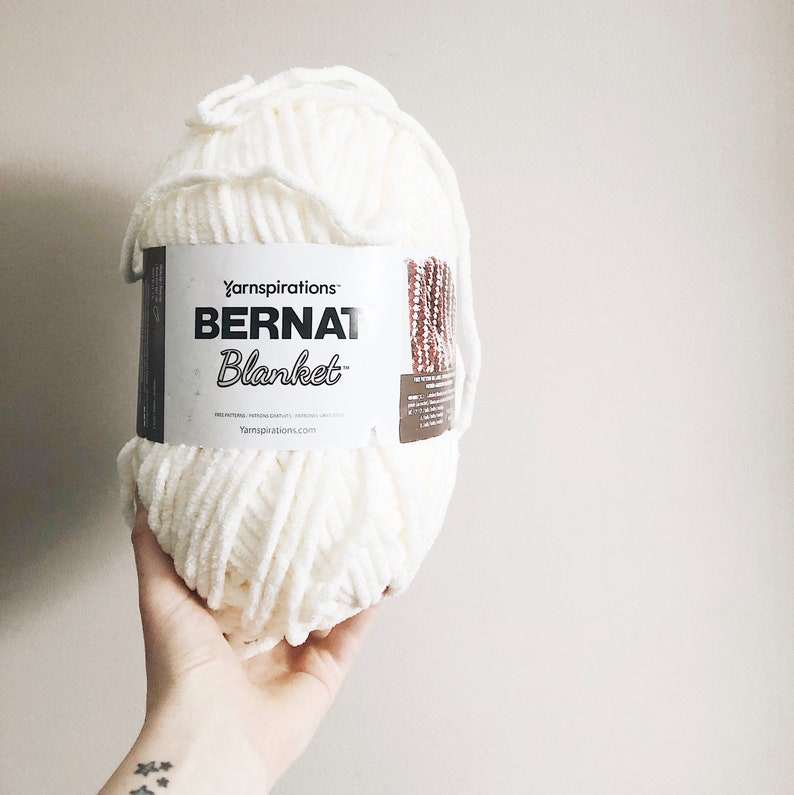 May include: A white ball of Bernat Blanket yarn by Yarnspirations. The label reads "Bernat Blanket" and "Yarnspirations.com".