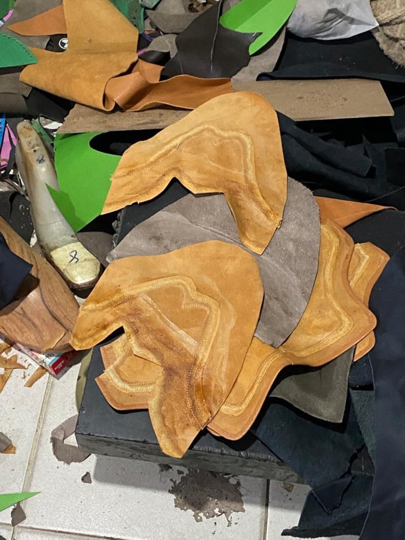 Puede incluir: Una colecci&oacute;n de piezas de cuero en varios colores, incluyendo marr&oacute;n, beige y negro. Las piezas parecen estar cortadas para componentes de zapatos, con costuras visibles y formas &uacute;nicas. Otros materiales tambi&eacute;n son visibles.