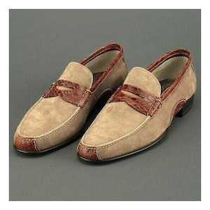 Puede incluir: Un par de mocasines de ante color beige con detalles en cuero marr&oacute;n. Los zapatos presentan un dise&ntilde;o de mocas&iacute;n con una correa de cuero marr&oacute;n y ribetes marrones. Las suelas son negras.