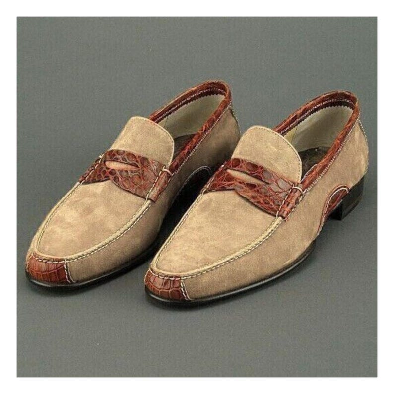 Puede incluir: Un par de mocasines de ante color beige con detalles en cuero marr&oacute;n. Los zapatos presentan un dise&ntilde;o de mocas&iacute;n con una correa de cuero marr&oacute;n y ribetes marrones. Las suelas son negras.