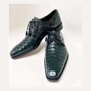 May include: A pair of dark green leather dress shoes with a crocodile pattern. The shoes have laces and a pointed toe.