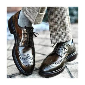 May include: A pair of brown leather wingtip dress shoes with a high-gloss finish. The shoes feature decorative perforations and are laced up with dark brown laces. The soles are dark brown, and the shoes are worn with gray socks and plaid trousers.