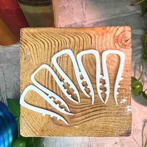 Op de afbeelding: Zes witte plastic clips, elk met een gebogen handvat en een gekerfde grijprand, liggen op een lichtbruin houten blok. De opstelling suggereert een knutsel- of organisatiethema.