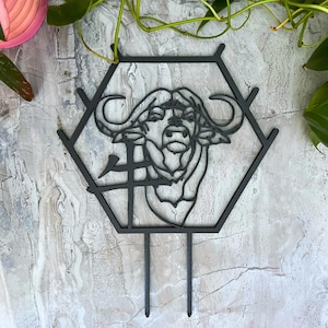 May include: Black metal garden stake featuring a bull's head within a hexagonal frame. The bull's head is a detailed line drawing. The stake has two prongs for easy insertion into the soil. The Chinese character for "ox" is also visible.