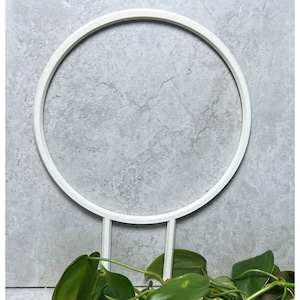 Könnte beinhalten: Weißer Metallring mit zwei vertikalen Stützen. Der Ring ist kreisförmig und die Stützen sind gerade. Der Ring hat einen Durchmesser von etwa 30 cm. Die Stützen sind etwa 15 cm hoch.