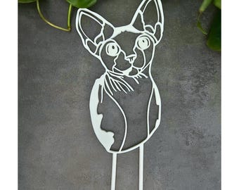 May include: A white cat-shaped cake topper with a Sphynx cat design. The topper features a detailed outline of the cat's face and body, with two vertical stakes for insertion into a cake. The cat's ears are large and pointed.