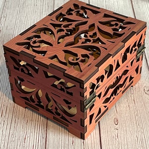 May include: A wooden box with a hinged lid and intricate floral cutouts. The box is made of a reddish-brown wood and has a natural wood grain finish.