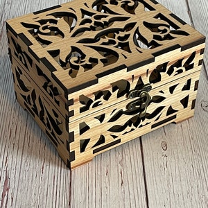 May include: A wooden box with a decorative, intricate floral design cut out of the lid. The box has a brown latch and is made of light wood.
