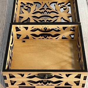 May include: A wooden box with a black trim and intricate cut-out designs. The box has a hinged lid and a metal latch.