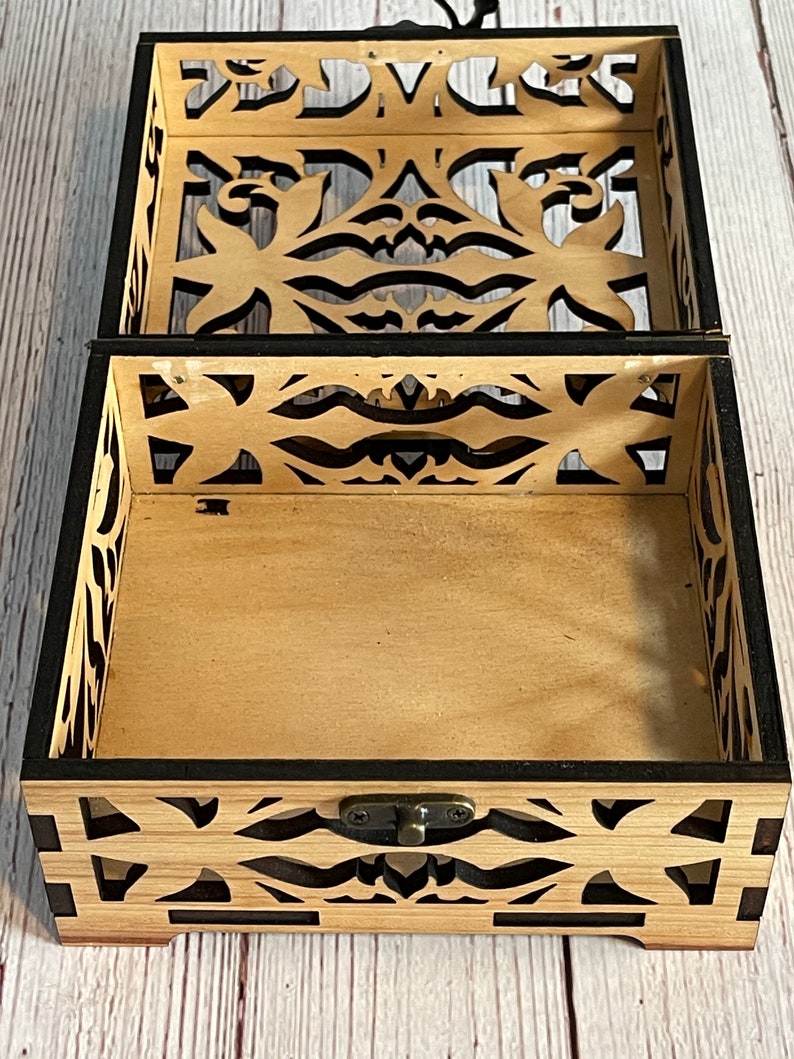May include: A wooden box with a black trim and intricate cut-out designs. The box has a hinged lid and a metal latch.