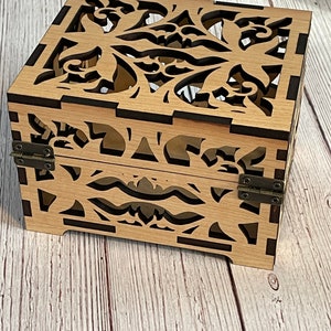 May include: A wooden box with a decorative floral design cut out of the sides and top. The box has a dark brown stain and is closed with two metal hinges.