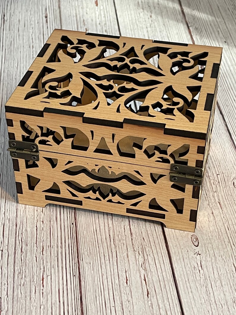 May include: A wooden box with a decorative floral design cut out of the sides and top. The box has a dark brown stain and is closed with two metal hinges.
