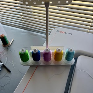 May include: A white plastic thread stand with six spools of thread. The spools are green, blue, pink, yellow, and light blue. The stand is labeled "POOLin".