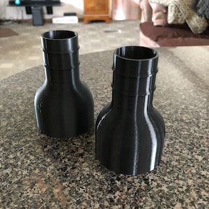 Puede incluir: Dos tapones de botella de plástico negro impresos en 3D con un diseño acanalado.