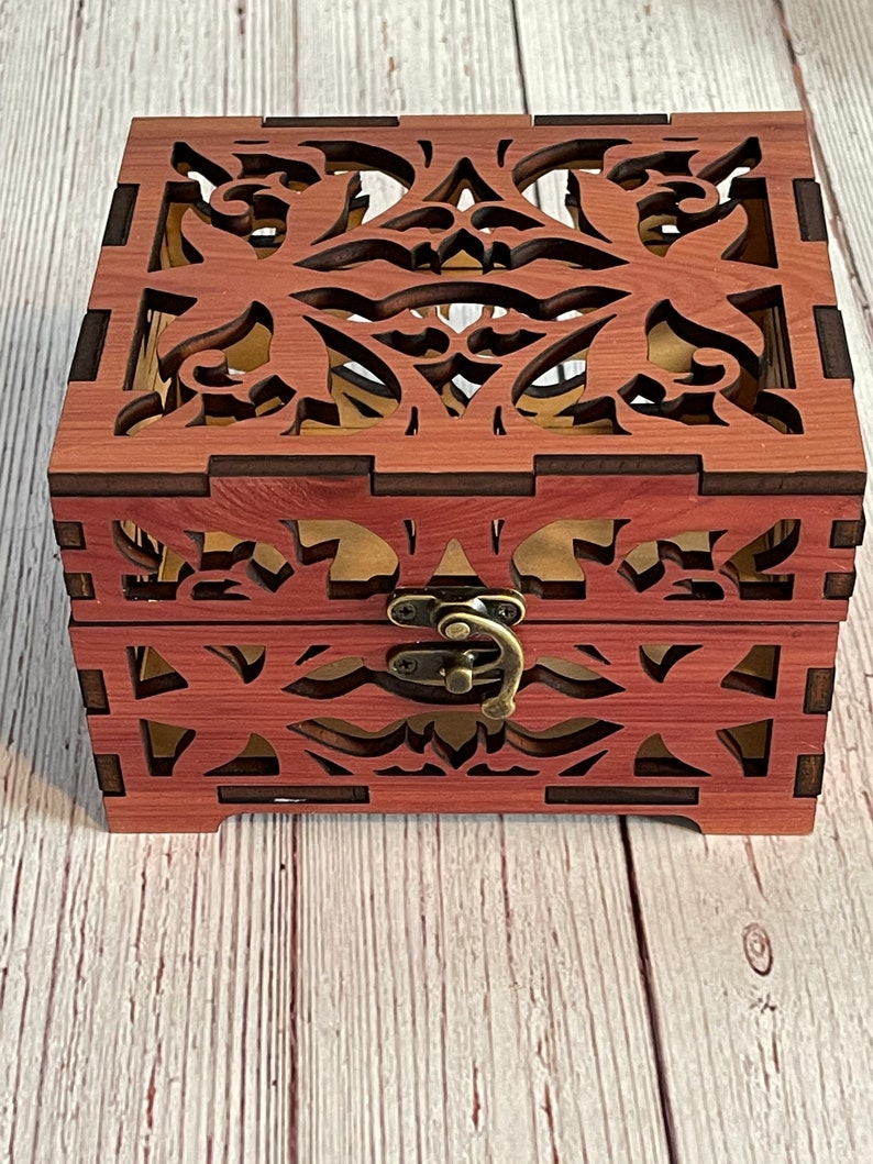 May include: A wooden box with a decorative, intricate, laser-cut design. The box has a hinged lid and a brass latch.