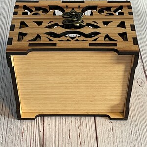 May include: A wooden box with a decorative cutout design and a brass latch. The box is closed and the lid is facing up.