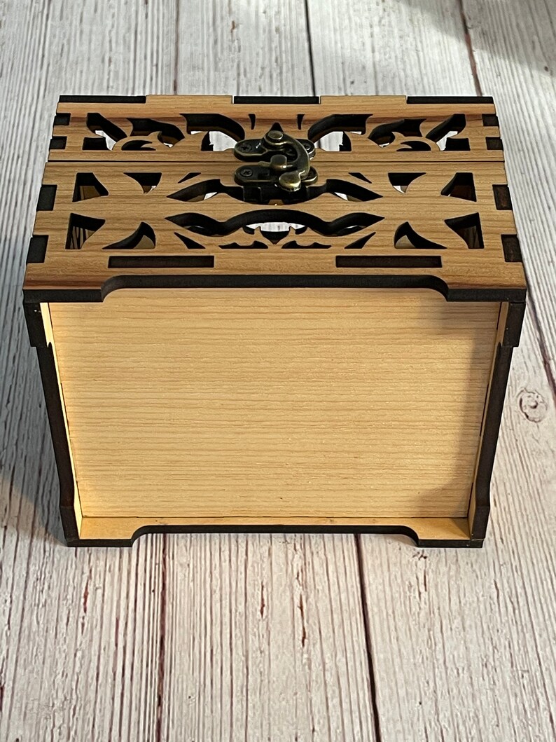 May include: A wooden box with a decorative cutout design and a brass latch. The box is closed and the lid is facing up.