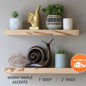 May include: Two floating shelves with wormy maple accents. The shelves hold decorative items, including potted plants, a gold hand sculpture, and a bronze snail. The shelves are 7 inches deep and 2 inches thick.
