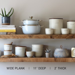 May include: Two rustic wooden shelves displaying kitchen and home decor items. Items include white pots and canisters labeled "Flour", "Sugar", "Salt", and "Pepper", along with a blue and white patterned pot, a small clock, and books. The shelves are 11 inches deep and 2 inches thick.