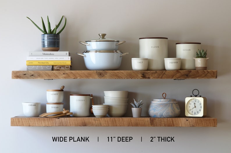 May include: Two rustic wooden shelves displaying kitchen and home decor items. Items include white pots and canisters labeled "Flour", "Sugar", "Salt", and "Pepper", along with a blue and white patterned pot, a small clock, and books. The shelves are 11 inches deep and 2 inches thick.