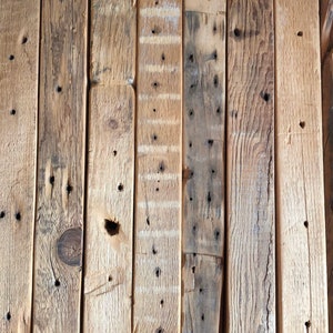 Puede incluir: Disposici&oacute;n vertical de tablones de madera reciclada. Los tablones var&iacute;an en color, desde marr&oacute;n claro hasta marr&oacute;n oscuro, con nudos, agujeros de clavos y vetas visibles. La madera tiene un aspecto envejecido.