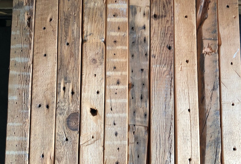 Puede incluir: Disposici&oacute;n vertical de tablones de madera reciclada. Los tablones var&iacute;an en color, desde marr&oacute;n claro hasta marr&oacute;n oscuro, con nudos, agujeros de clavos y vetas visibles. La madera tiene un aspecto envejecido.
