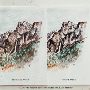 May include: Two watercolor prints of a mountain landscape, one on textured paper and one on smooth paper. The artwork depicts a mountain range with a waterfall, trees, and a small building. The prints are labeled "TEXTURED PAPER" and "SMOOTH PAPER".