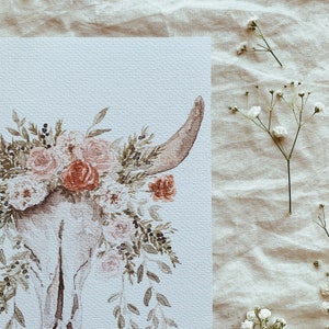 May include: A watercolor painting of a white animal skull with a floral crown of pink and red flowers. The background is a light beige.