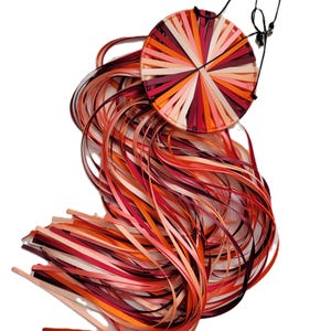 May include: A Snappy Dragontail 6" Ring, featuring a circular design with radiating strips in shades of red, orange, and pink. Long, flowing ribbons of matching colors cascade from the ring, creating a dynamic visual effect. A black cord and ring are attached.